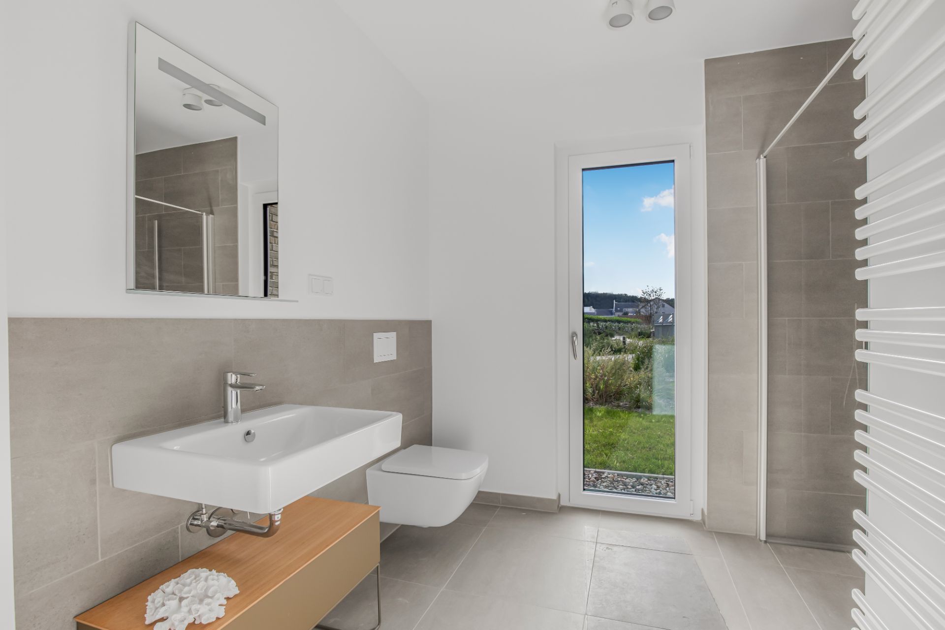 Modernes Badezimmer mit Waschbecken, Wandtoilette und großer Glastür zum Garten.