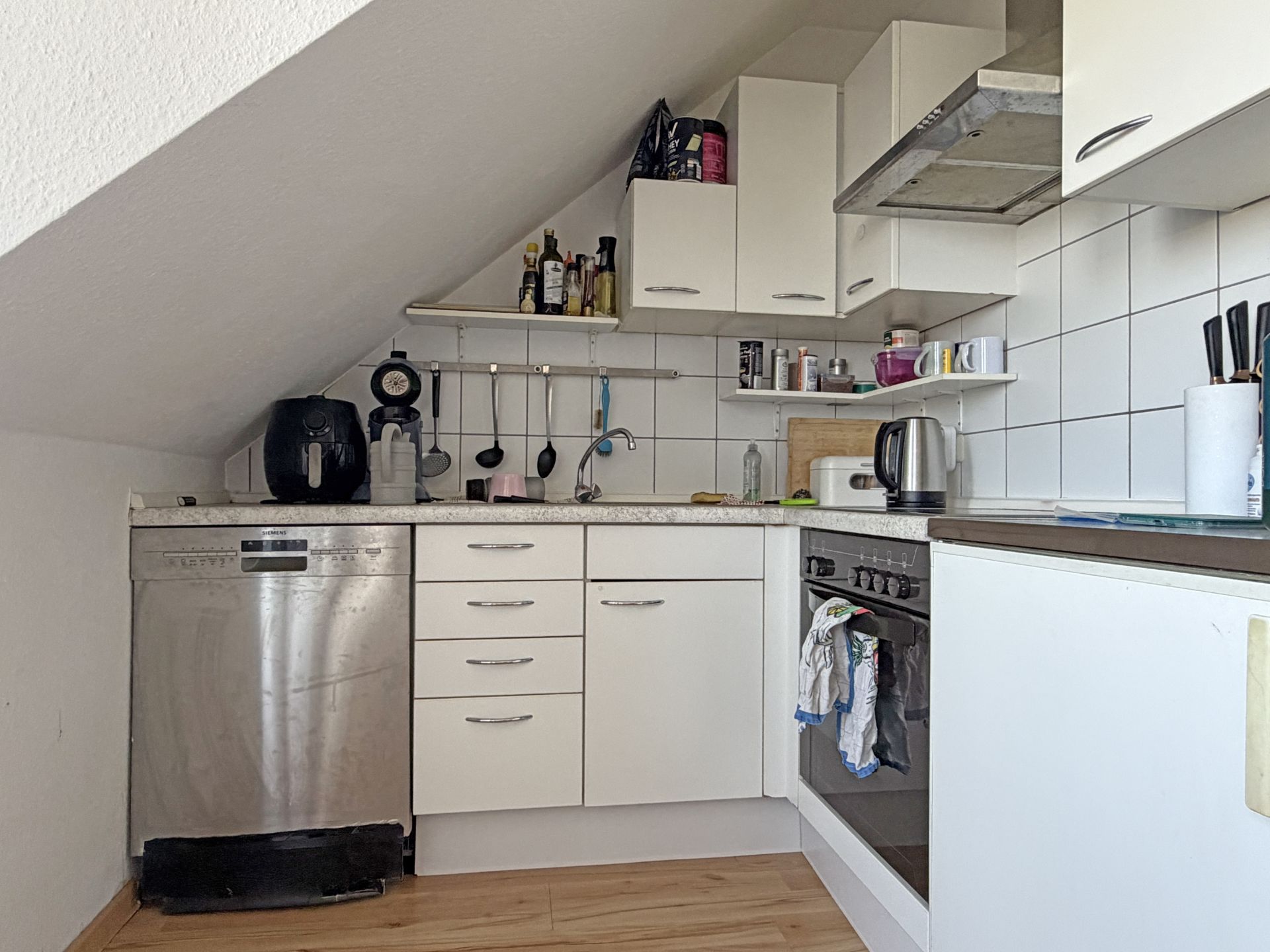 Helle Einbauküche mit Dachschräge, Spülmaschine, Herd, Spüle und Küchenutensilien.