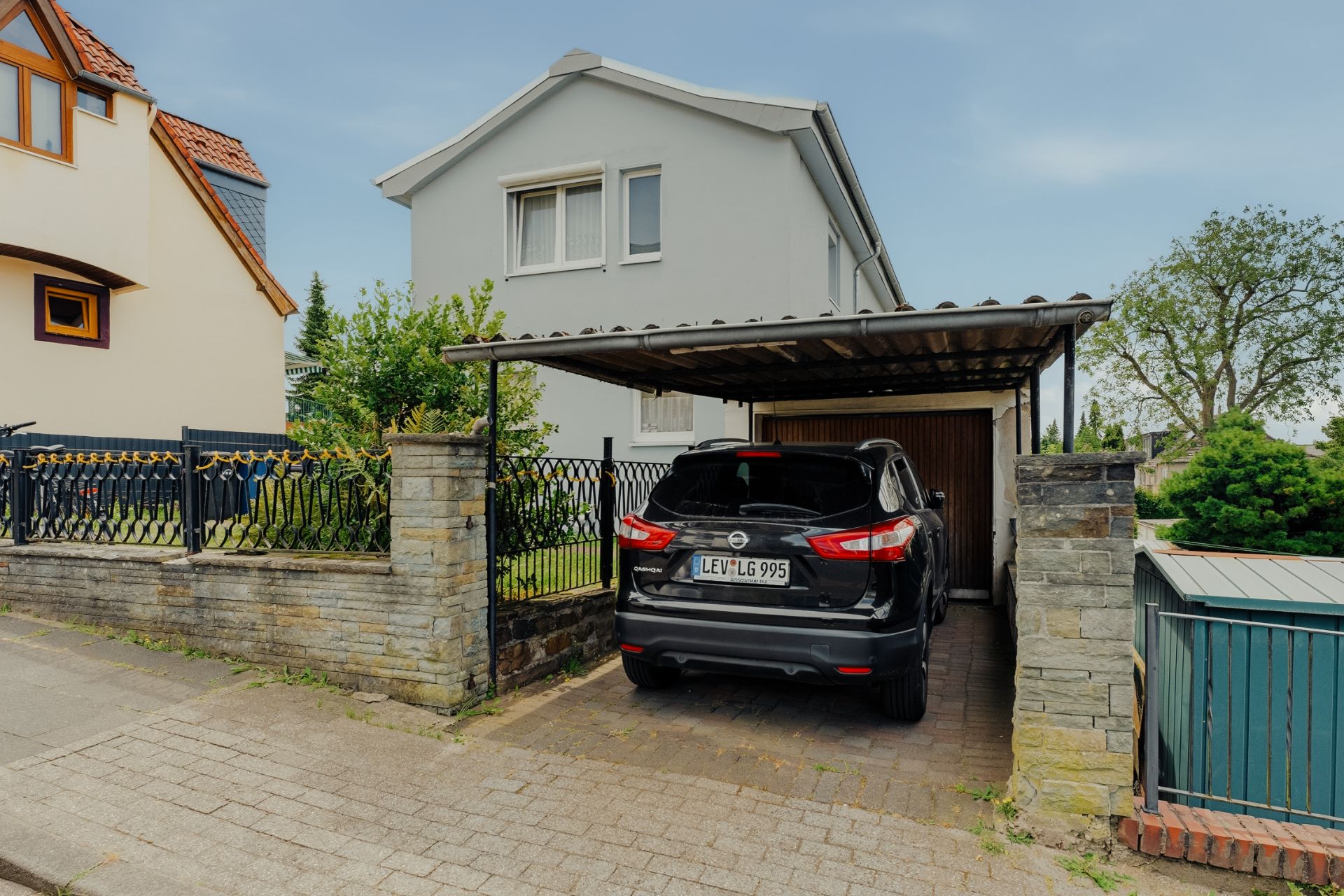Haus mit Carport und geparktem schwarzen Auto in einer Wohnstraße.