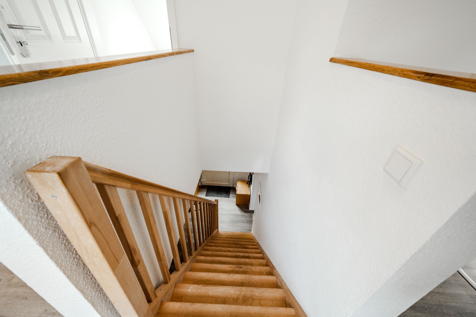 Holztreppe mit Geländer führt vom Obergeschoss in ein helles Zimmer.