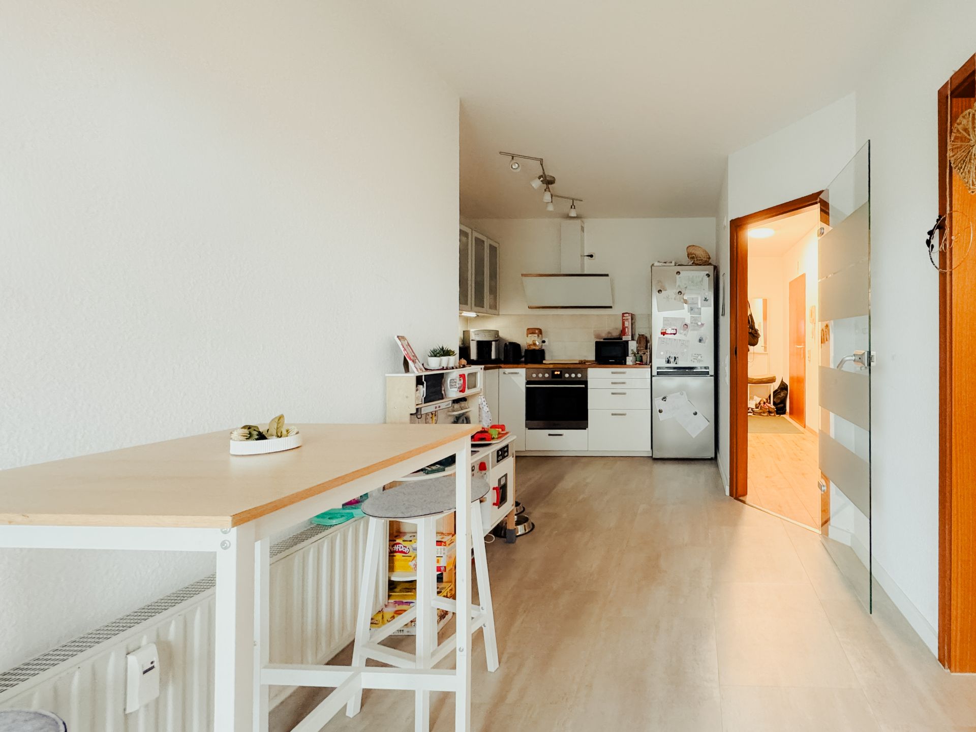 Helle Küche mit Esstisch, Hockern, Herd, Kühlschrank und weißem Boden.