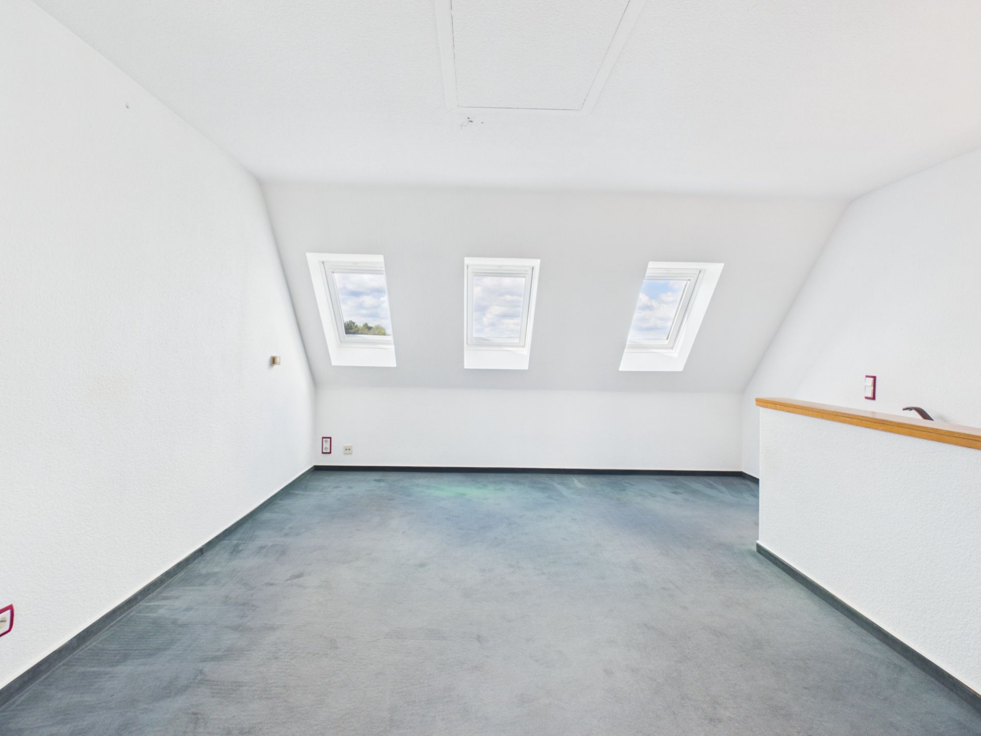 Heller Raum mit drei Dachfenstern und blauem Teppichboden.