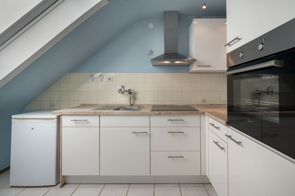 Moderne Einbauküche mit weißem Kühlschrank, Herd, Spüle und Backofen unter einer Dachschräge.