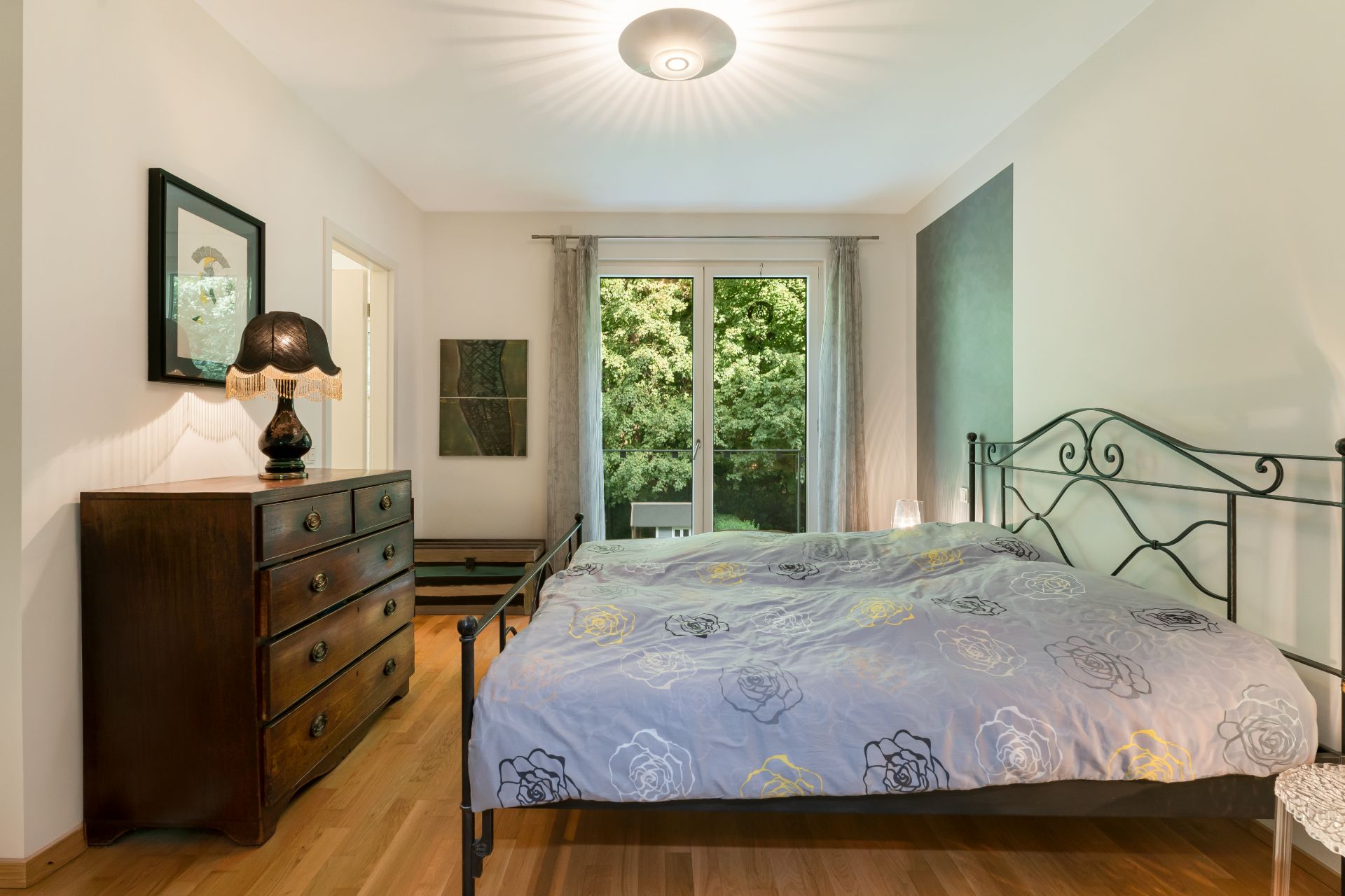 Schlafzimmer mit Doppelbett, Kommode und Fenster mit Blick ins Grüne.
