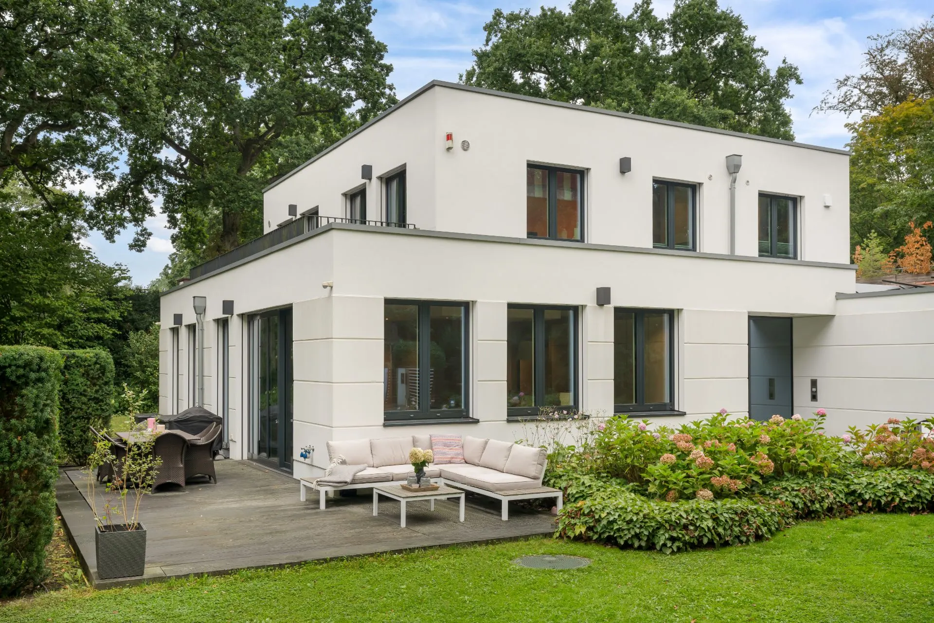 Modernes zweistöckiges Haus mit Terrasse, Gartenmöbeln und Garten im Vordergrund.