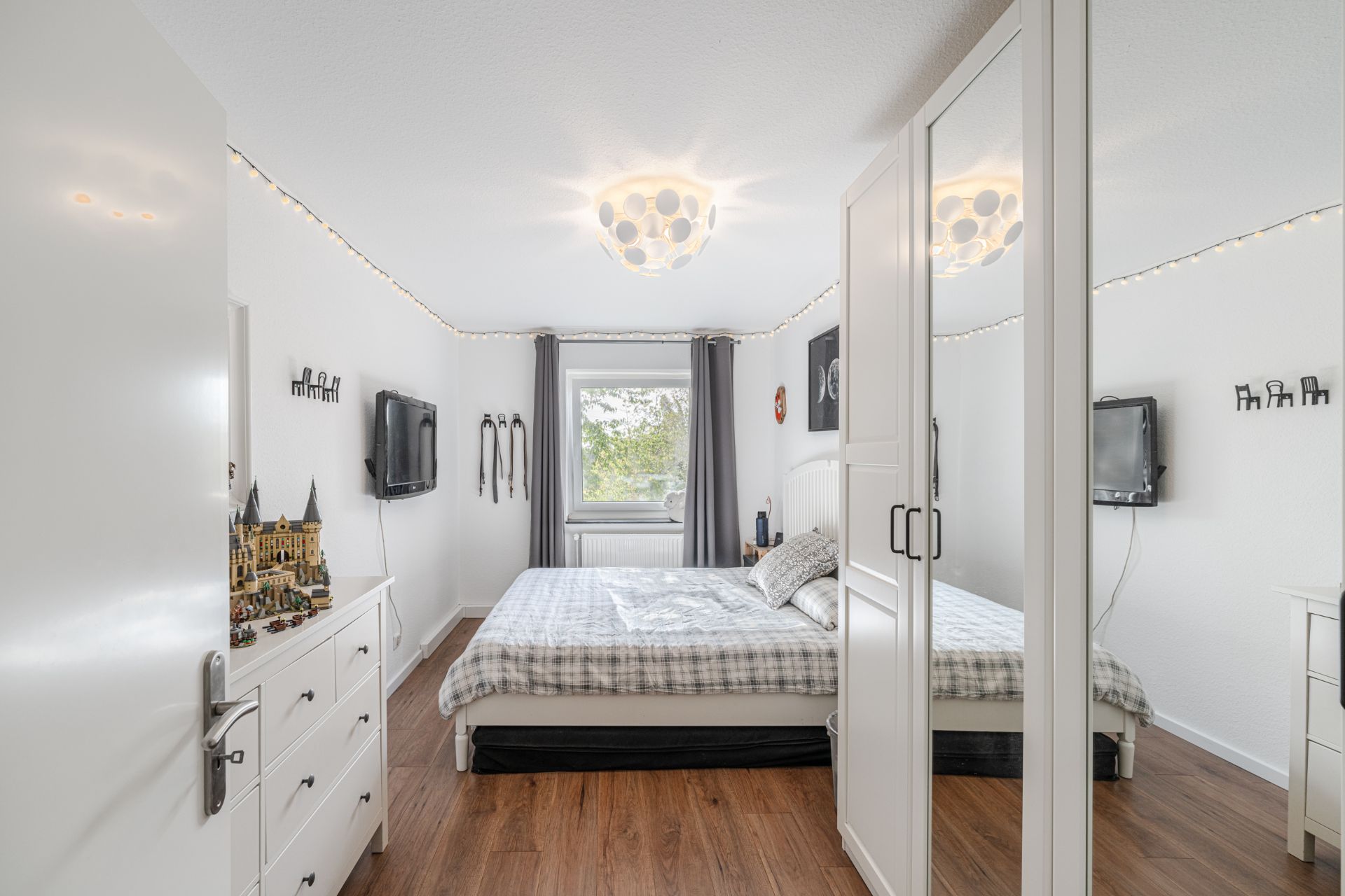 Helles Schlafzimmer mit großem Bett, Spiegelkleiderschrank und Fernseher an der Wand.