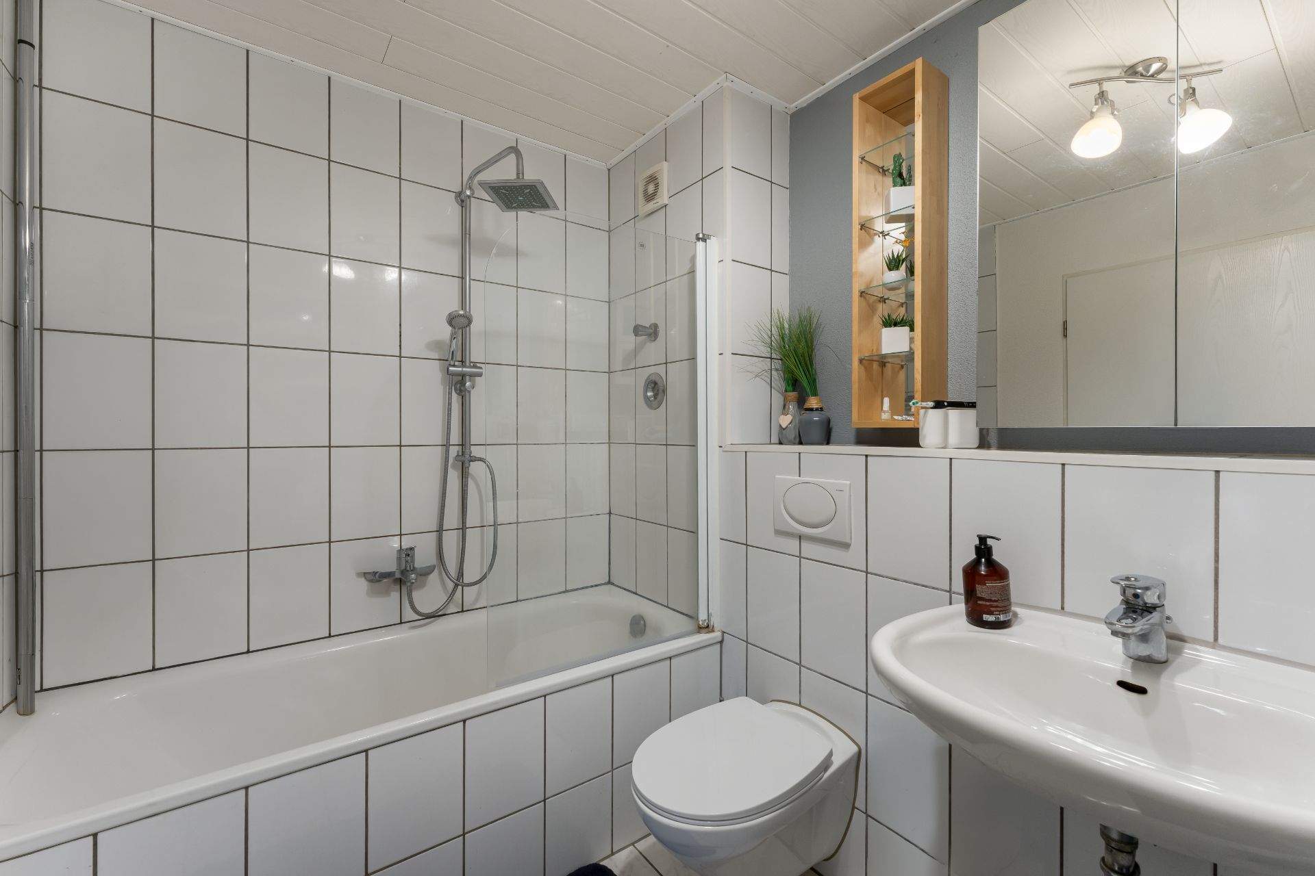 Modernes Badezimmer mit Badewanne, Dusche, Waschbecken und WC, weiße Fliesen an Wand und Boden.