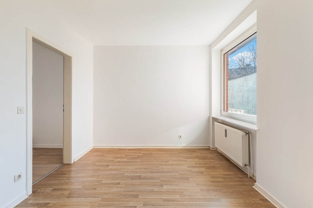 Heller leerer Raum mit Holzfußboden und großem Fenster, Heizkörper unter dem Fenster.
