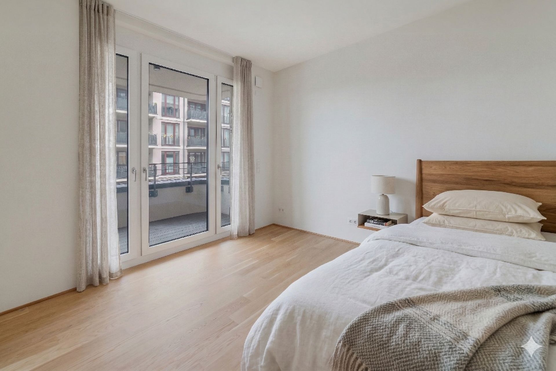 Helles Schlafzimmer mit Holzboden, Bett, Nachttisch und großen Fenstern zum Balkon.