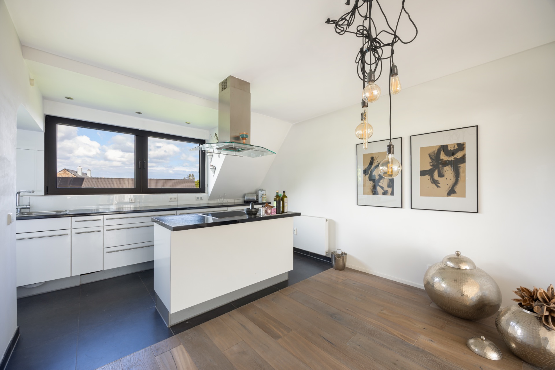 Moderne Küche mit Kochinsel, großem Fenster, Holzboden und dekorativen Bildern an der Wand.