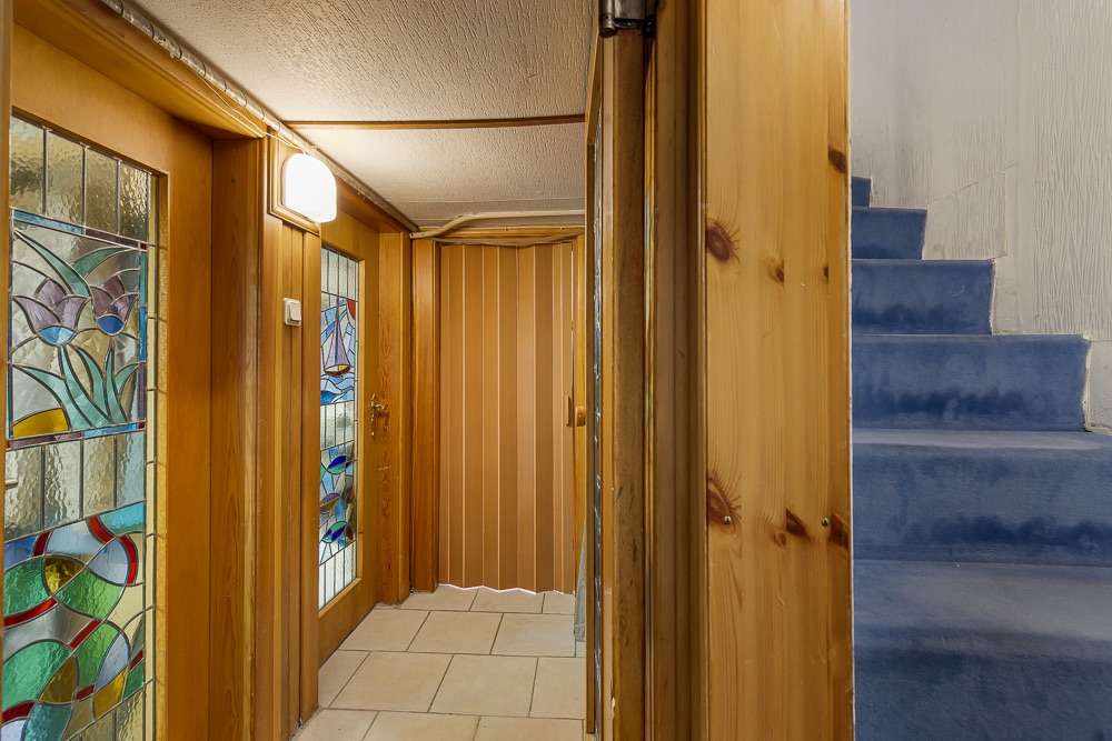 Flur mit Holzverkleidung, Glastüren mit buntem Muster und blauer Treppe nach oben.