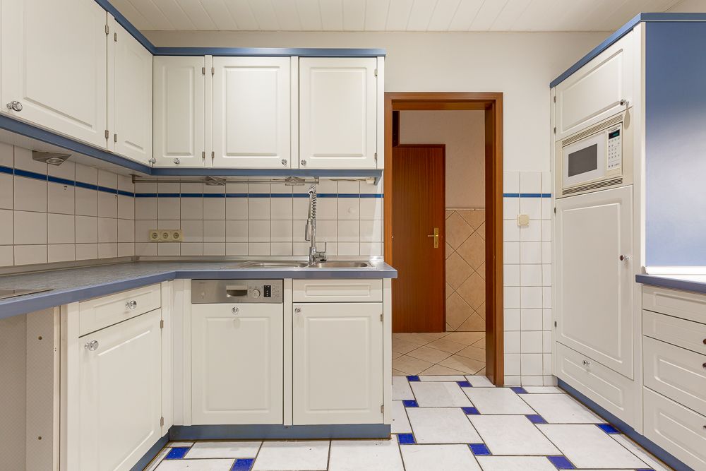 Helle Einbauküche mit weißen Schränken, blauen Akzenten und Fliesenboden.