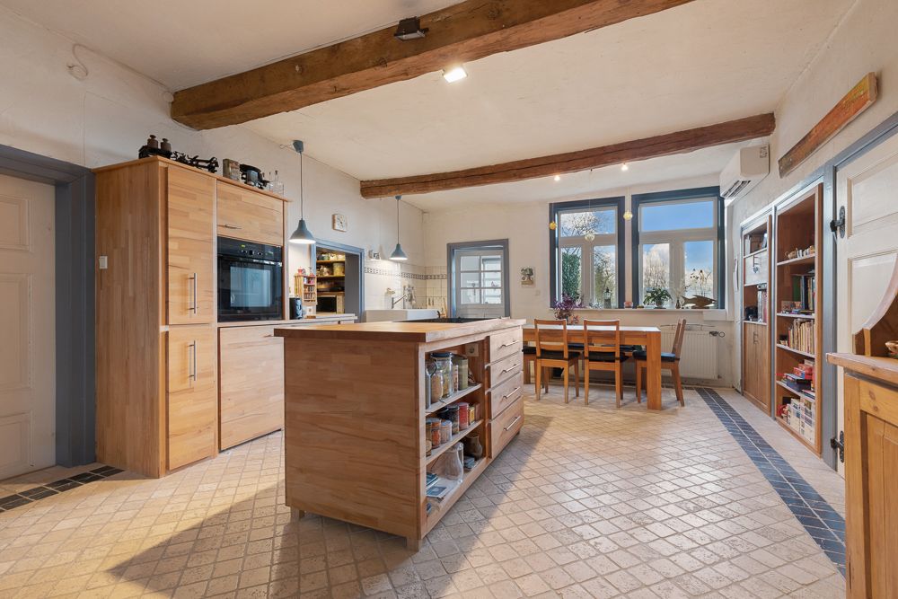 Große Wohnküche mit Holzmöbeln, Esstisch, Kücheninsel und sichtbaren Holzbalken an der Decke.