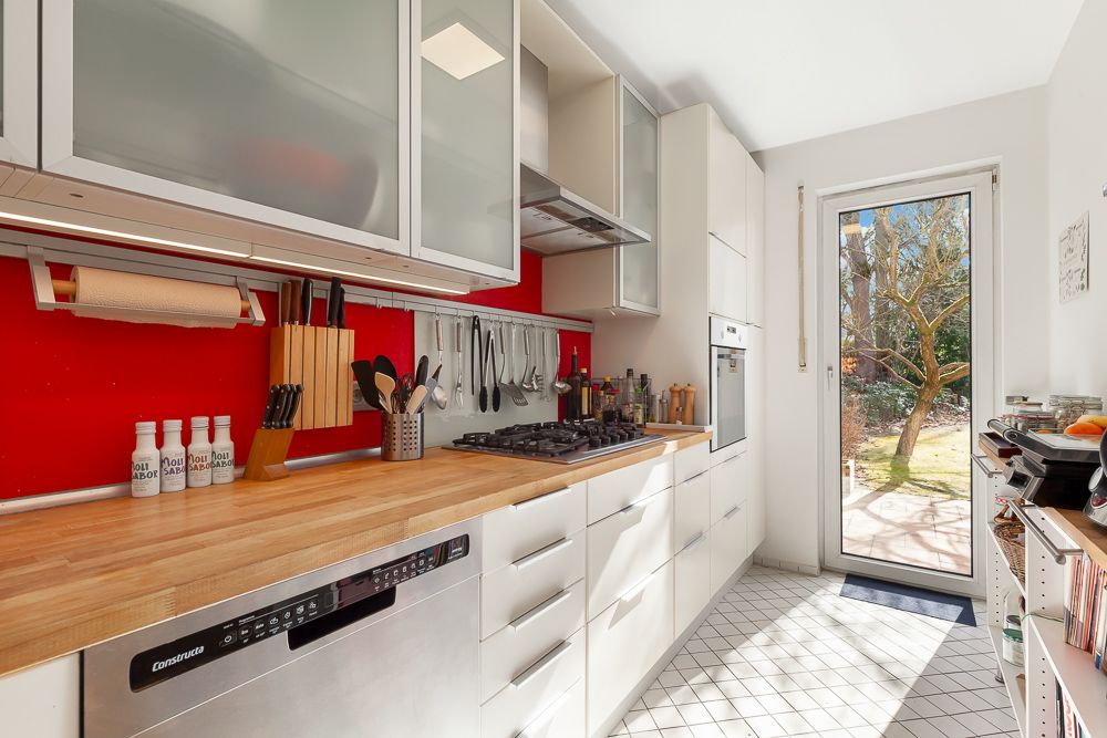 Moderne Küche mit Holzarbeitsplatte, weißen Schränken und roter Wand. Tür führt in den Garten.