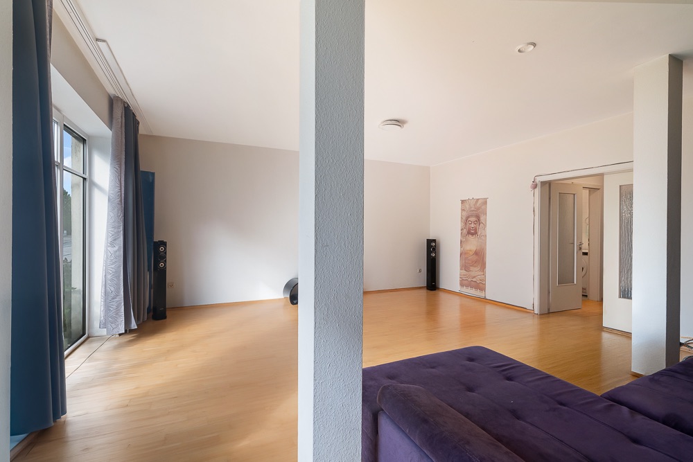 Großes Wohnzimmer mit Holzfußboden, lila Sofa und großen Fenstern mit Vorhängen.