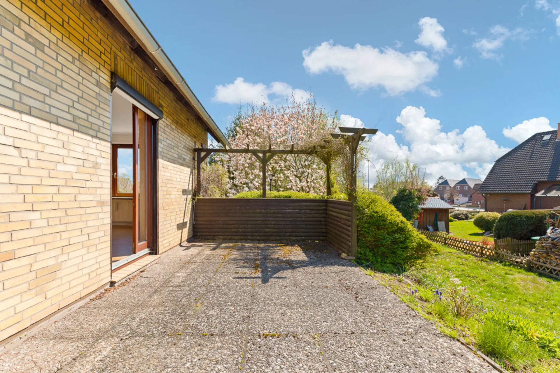 Terrasse mit Steinboden an einem Wohnhaus, Zugang durch offene Tür, Garten im Hintergrund.