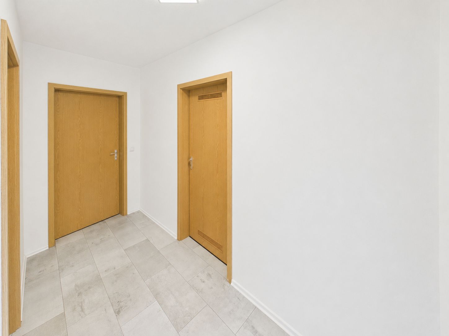 Heller Flur mit drei Holztüren und weißen Wänden in einer Wohnung.