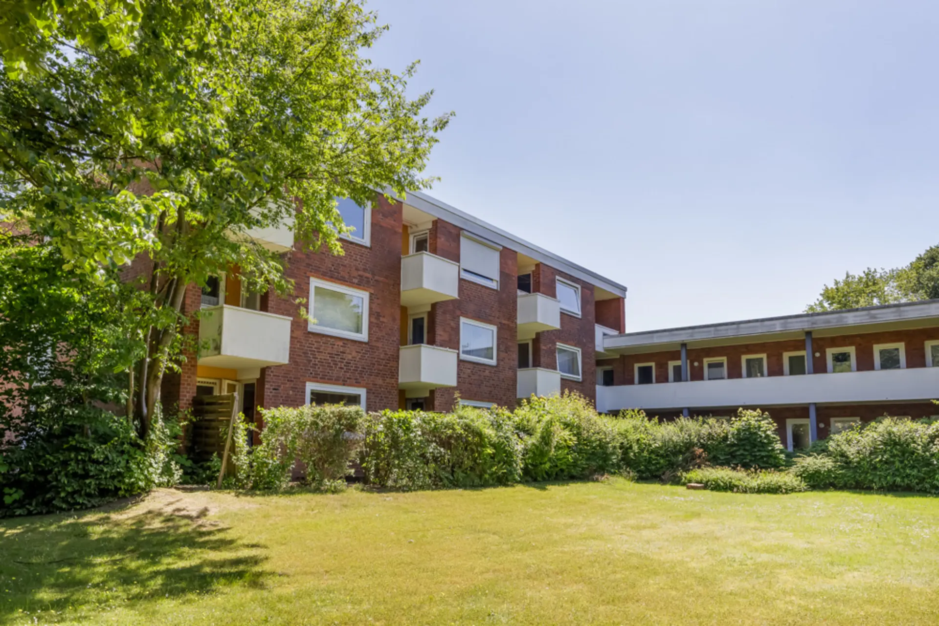 Mehrfamilienhaus aus rotem Backstein mit Balkonen und gepflegtem Garten im Vordergrund.