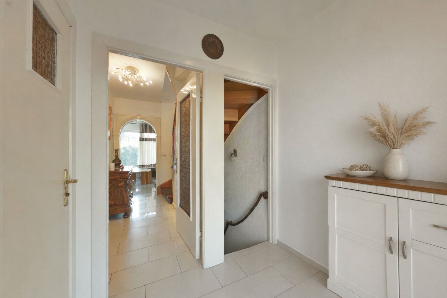Heller Flur mit weißen Türen, Treppe und Kommode mit Vase auf der rechten Seite.