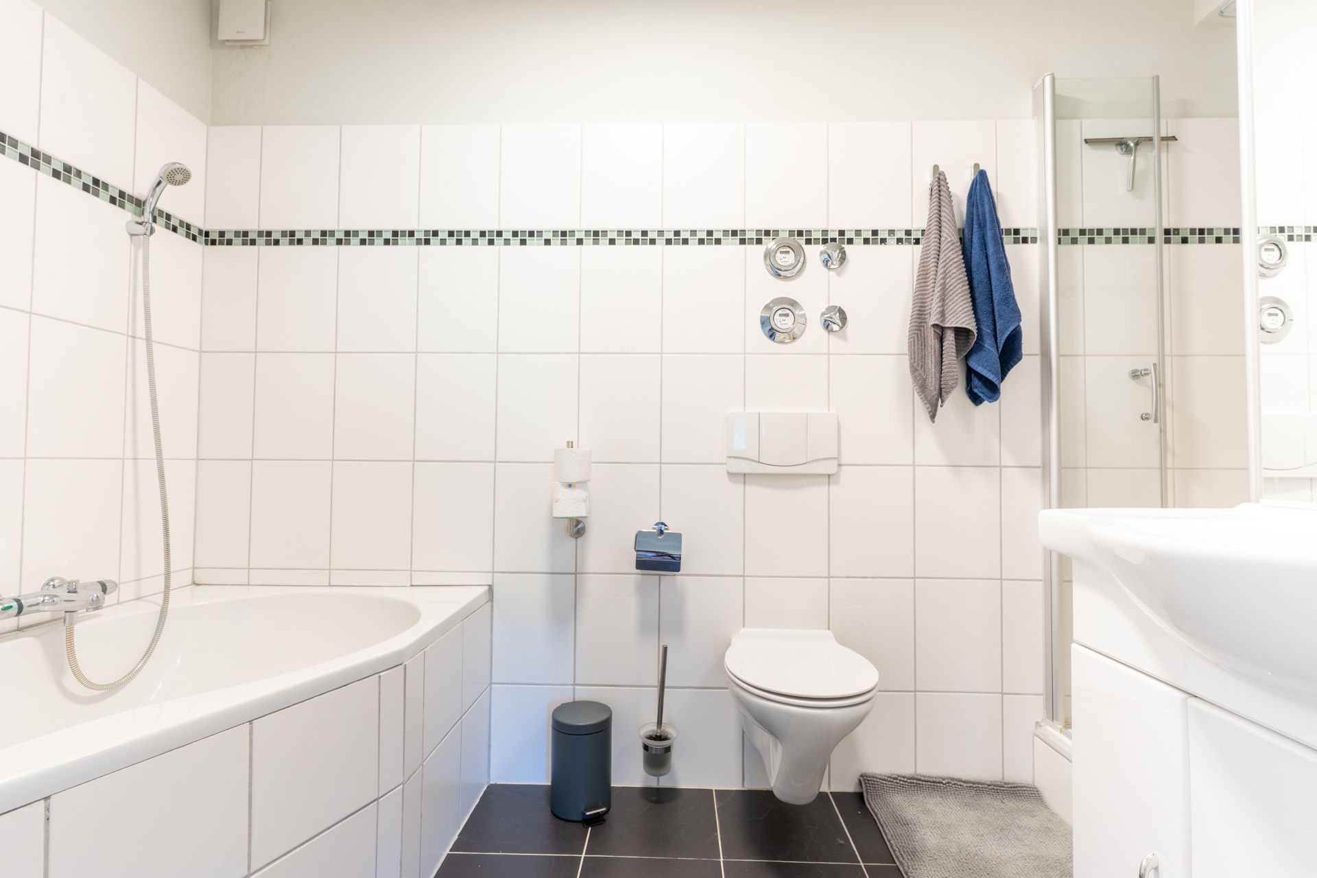 Helles Bad mit Badewanne, Dusche, WC und weißen Fliesen.