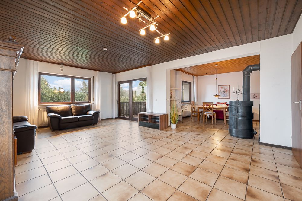 Großes Wohnzimmer mit Sitzbereich, Esstisch, Holzdecke, Fliesenboden und großen Fenstern.