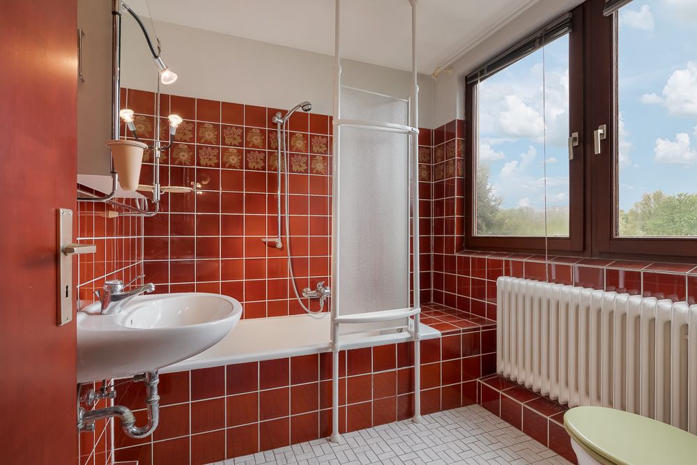 Badezimmer mit roten Fliesen, Badewanne, Duschvorhang, Waschbecken und großem Fenster.
