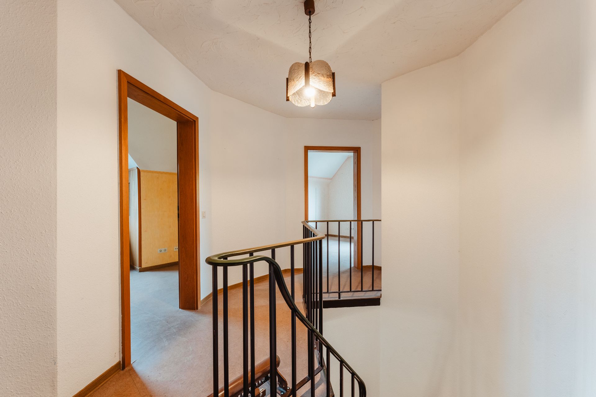 Treppenhaus mit Holzhandlauf, zwei offene Türen und Deckenlampe in einem Wohnhaus.