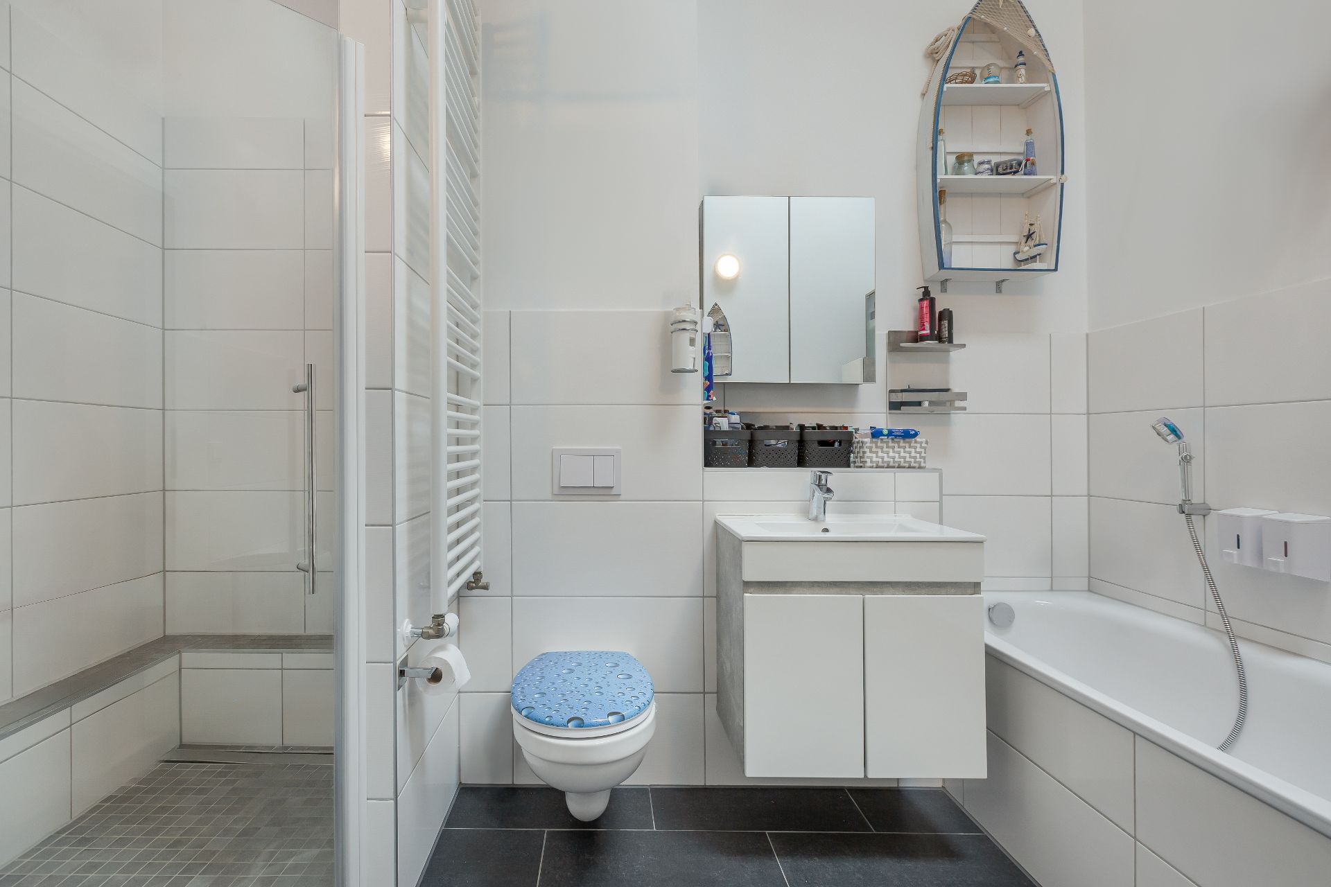 Modernes Badezimmer mit Dusche, Badewanne, Waschbecken und WC. Weiße Fliesen und Spiegel mit Ablage.