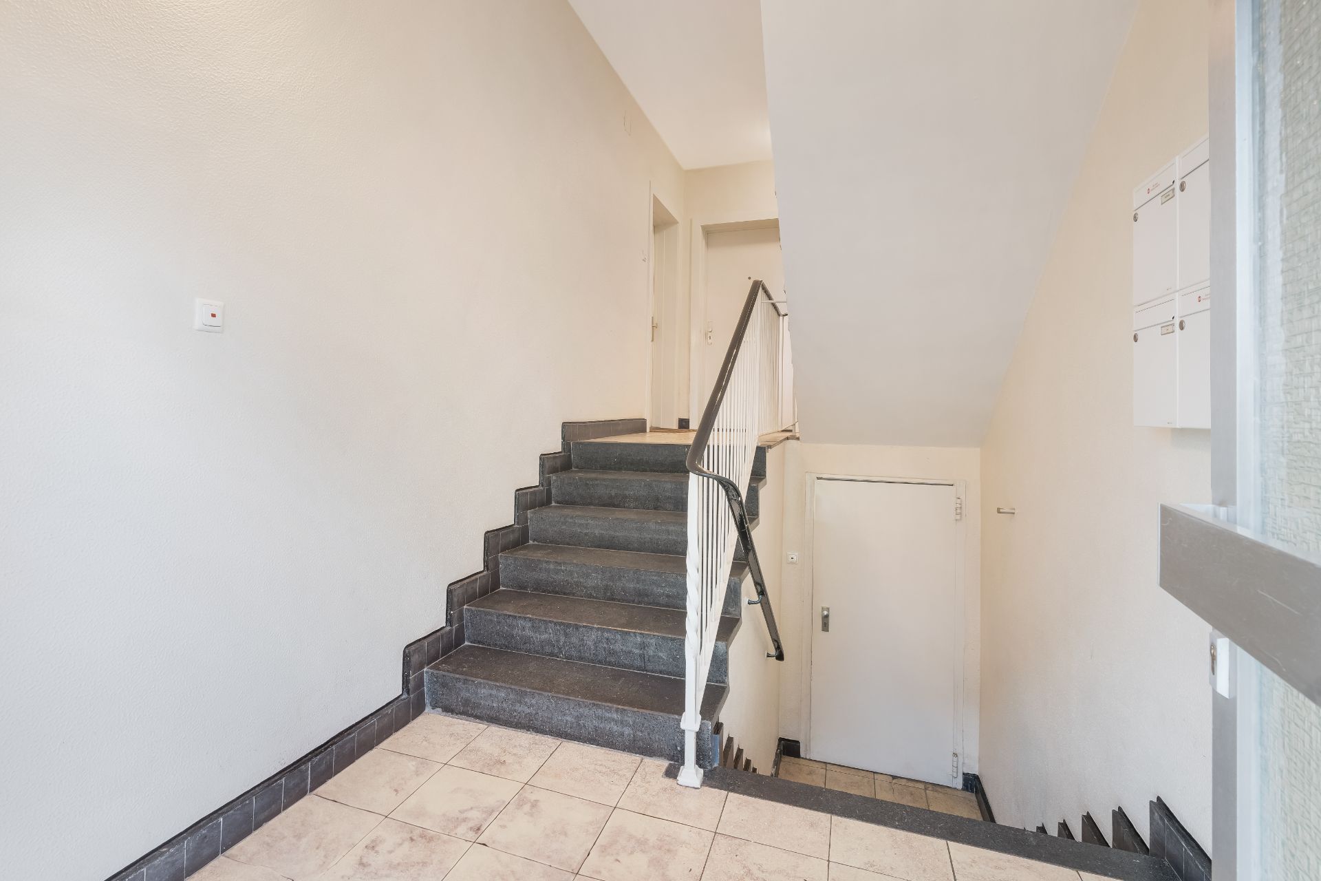 Treppenhaus mit gefliesten Bodenfliesen, Treppe und weißen Wänden in einem Wohngebäude.