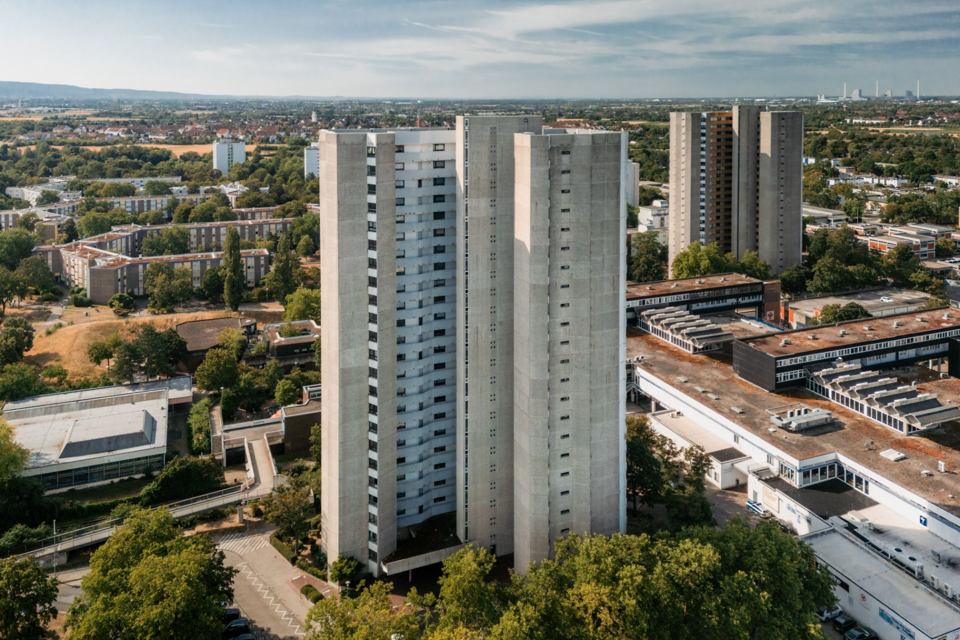 Hohes Wohngebäude mit mehreren Balkonen, umgeben von Bäumen und anderen Gebäuden.