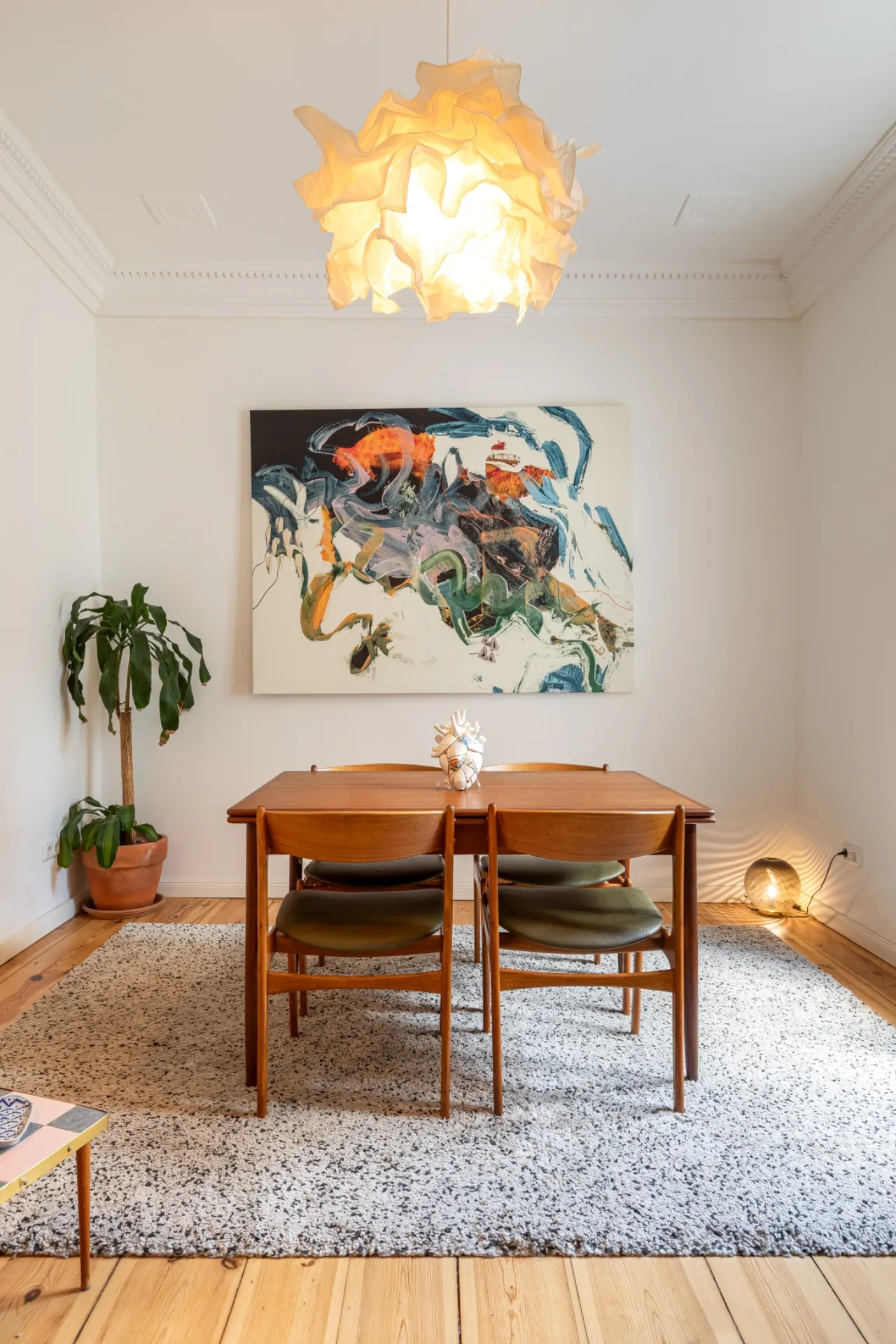 Esszimmer mit Holztisch, vier Stühlen, Teppich, moderner Lampe und abstraktem Bild an der Wand.
