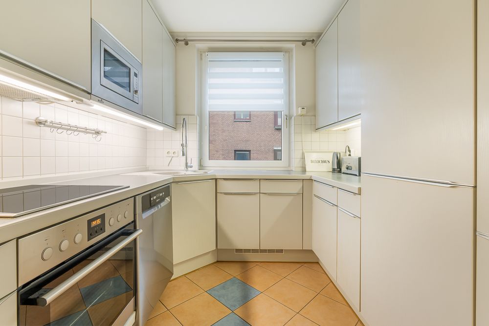Moderne Einbauküche mit weißen Schränken, Elektrogeräten und Fenster.
