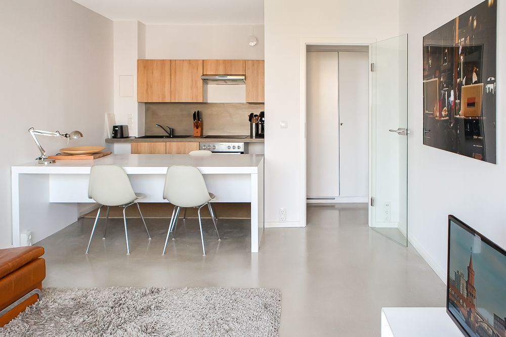 Moderne Wohnküche mit weißem Tisch, zwei Stühlen, Holzeinbauküche und Fernseher im Wohnzimmer.