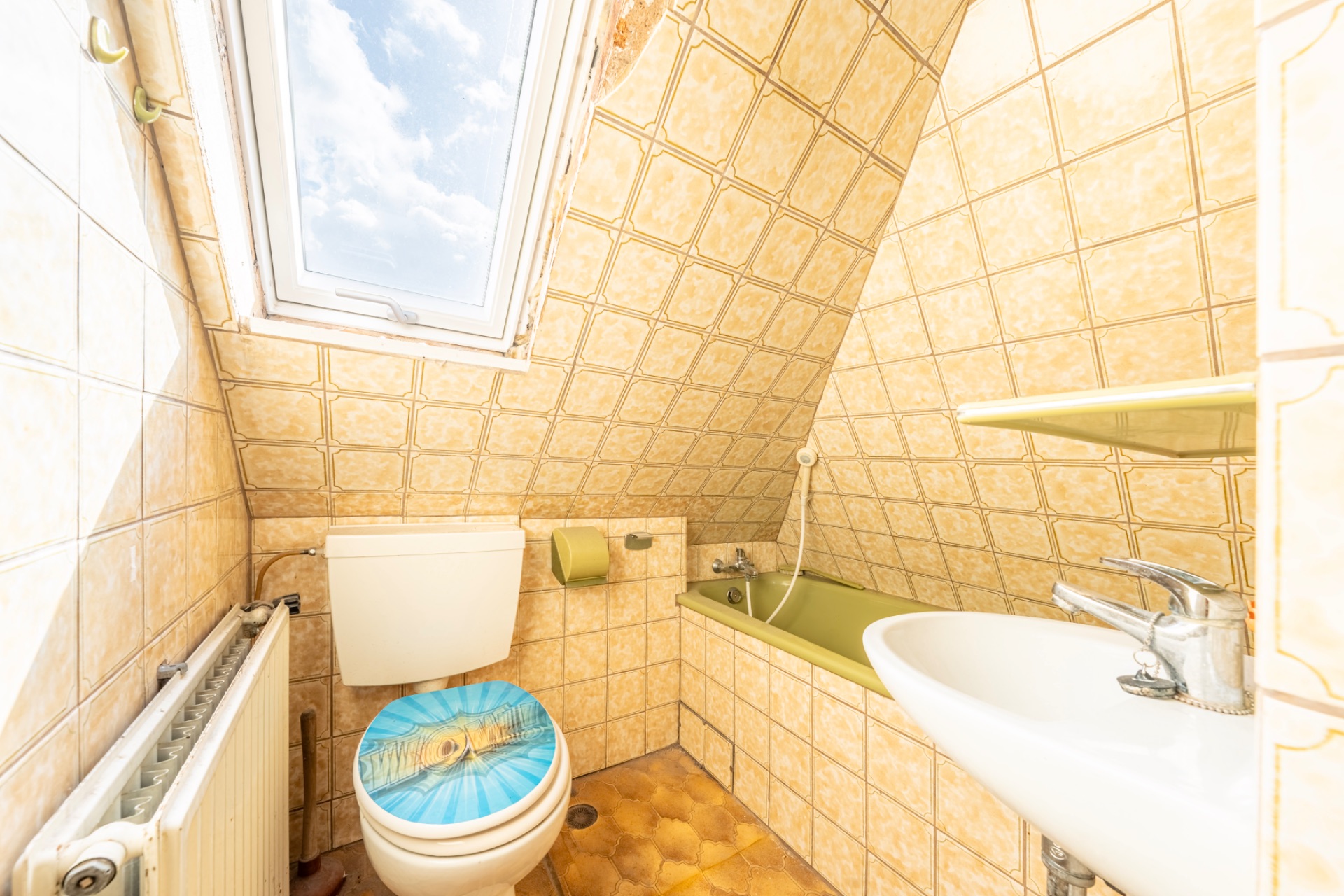Kleines Badezimmer mit Toilette, Badewanne, Waschbecken und Dachfenster.