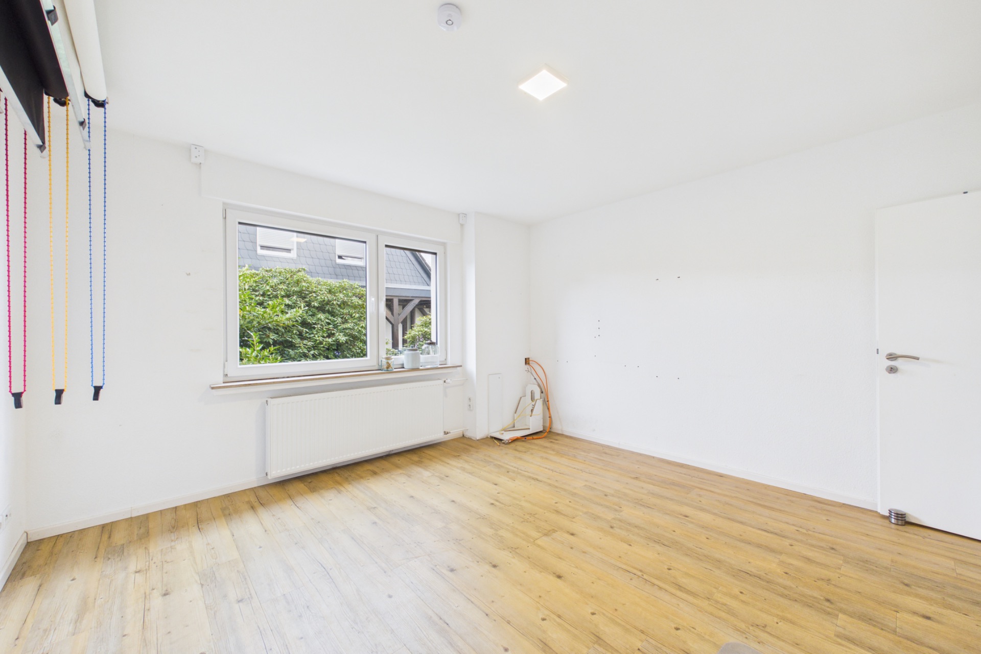 Heller, leerer Raum mit Holzboden, weißem Fenster und weißer Wand.