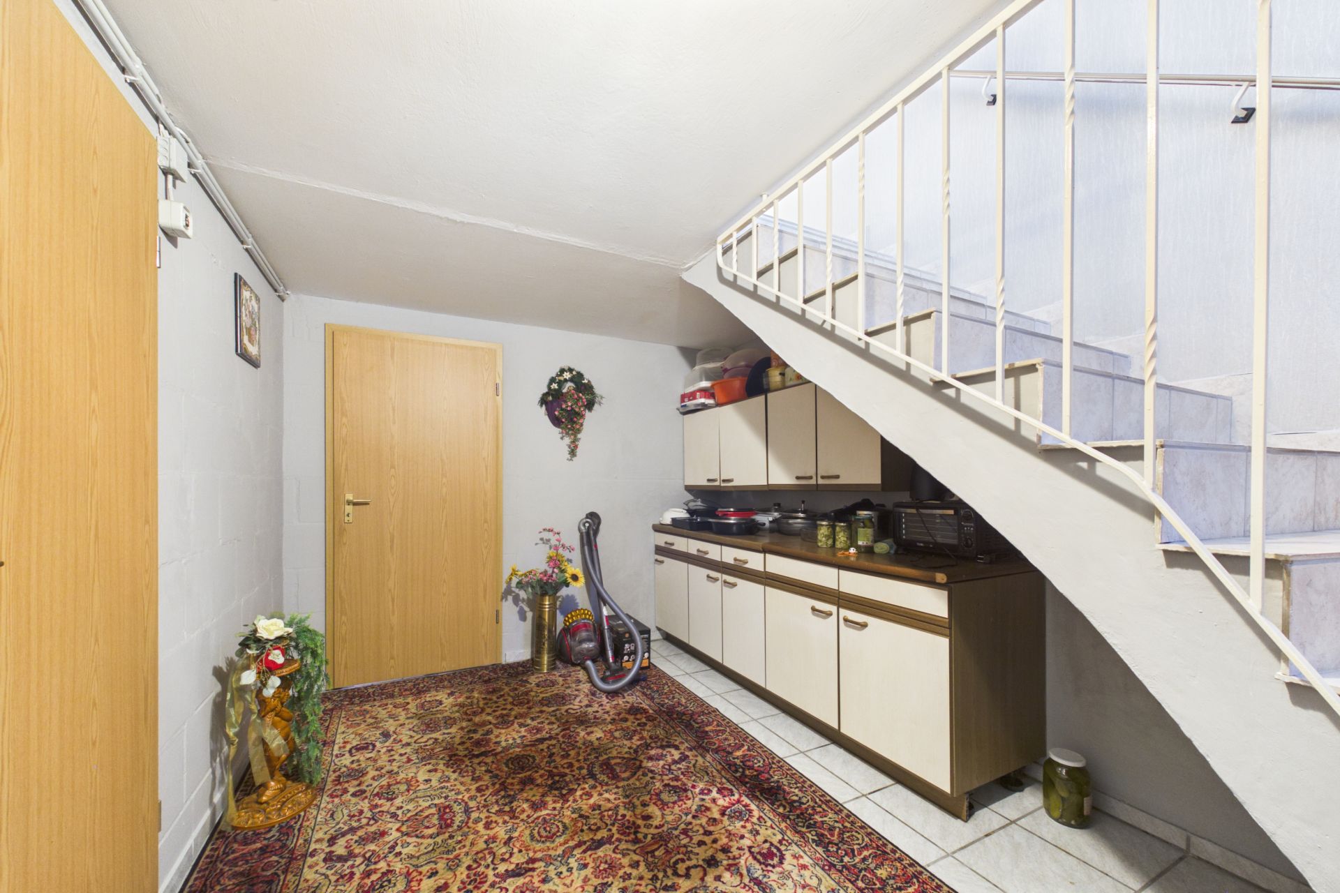 Flur mit Treppe, Teppich, Kommode, Staubsauger und Dekorationen an den Wänden.