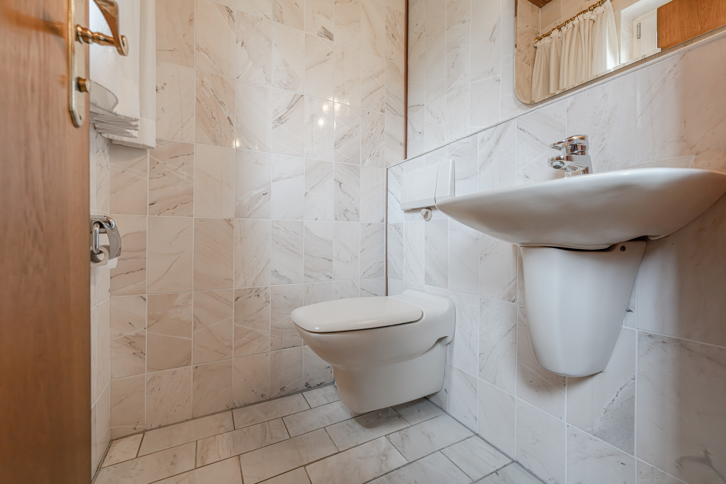 Kleines Badezimmer mit Wandtoilette, Waschbecken und Fliesen an Wand und Boden.