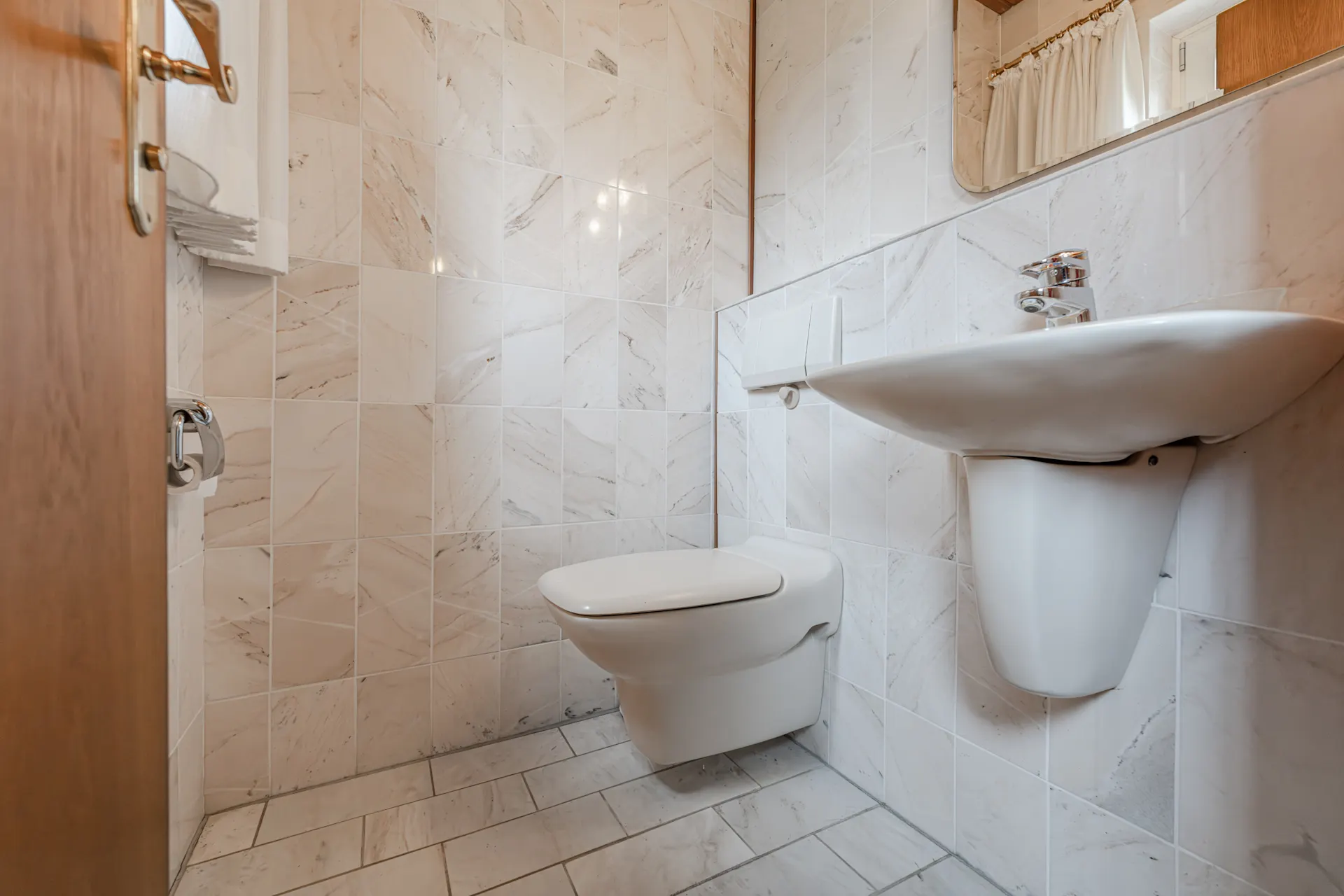 Kleines Badezimmer mit Wandtoilette, Waschbecken und Fliesen an Wand und Boden.