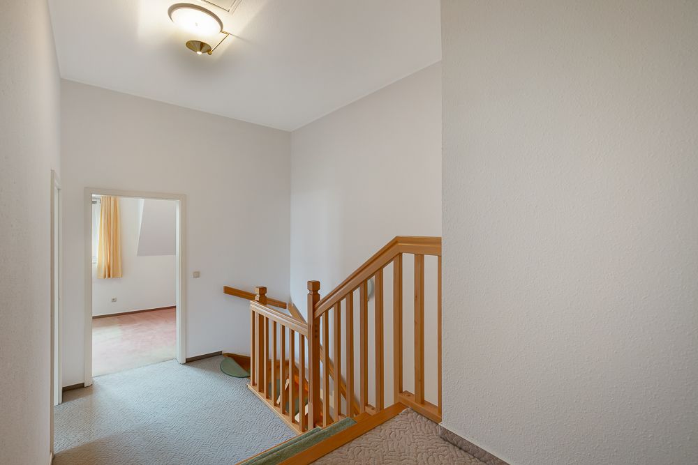 Heller Flur mit Treppe und Holzgeländer, Tür zu einem Zimmer mit Fenster und Vorhang.