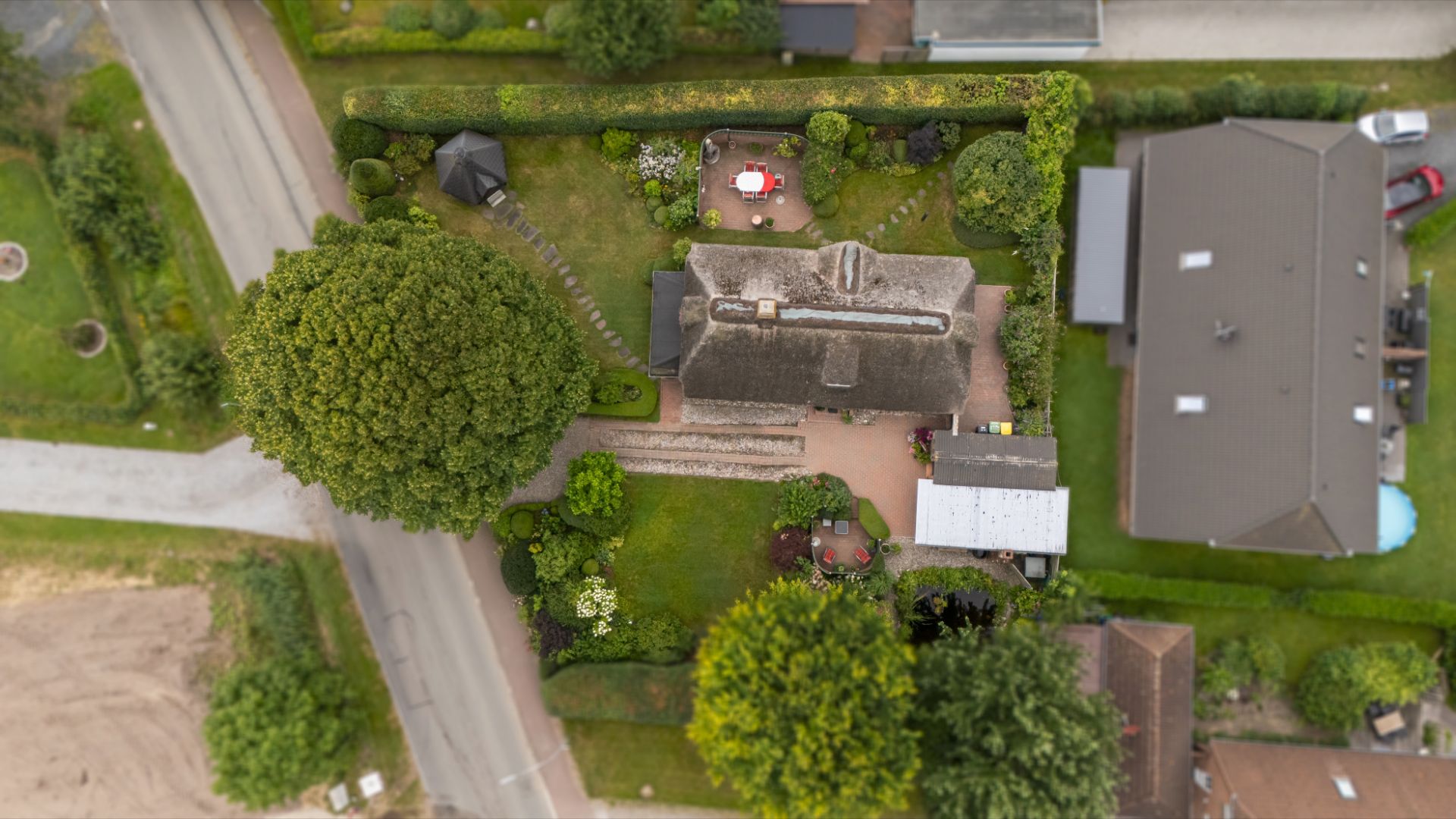 Luftaufnahme eines Hauses mit Garten, Bäumen und Terrasse in einer Wohnsiedlung.