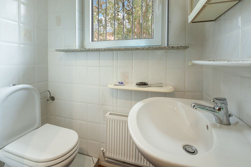 Kleines Badezimmer mit Toilette, Waschbecken, Fenster und weißen Fliesen.
