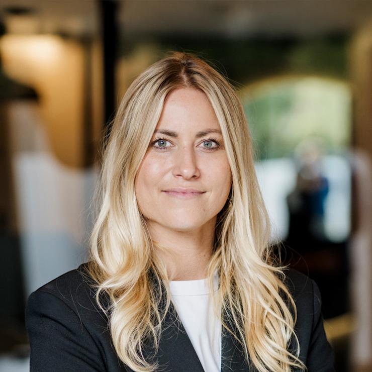 Junge Frau mit langen blonden Haaren steht mit verschränkten Armen draußen.