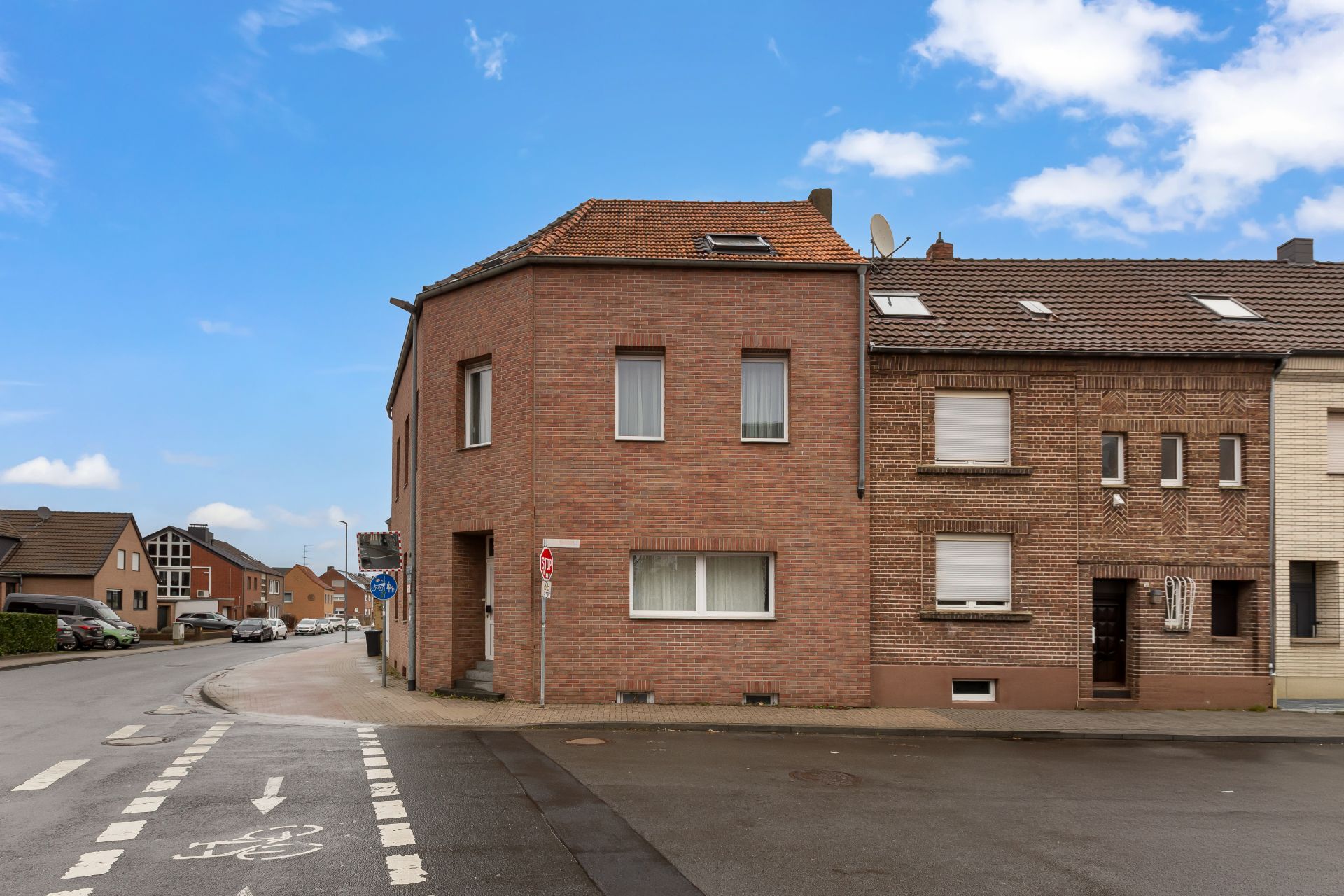 Backsteinhaus an einer Straßenecke mit mehreren Fenstern und Fahrradweg vor dem Gebäude.