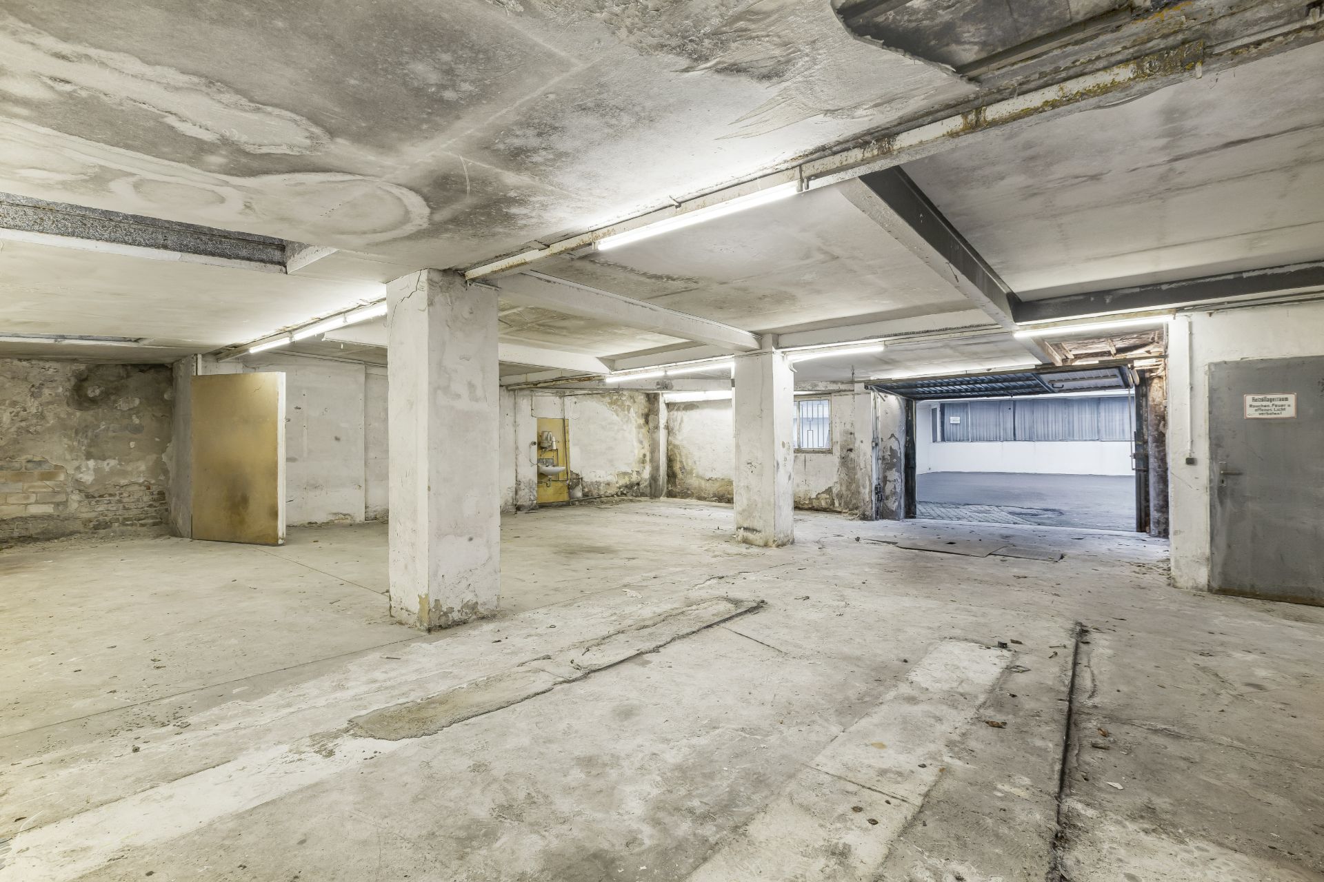 Geräumige, leere Garage oder Keller mit Betonboden, Säulen und offenem Garagentor.