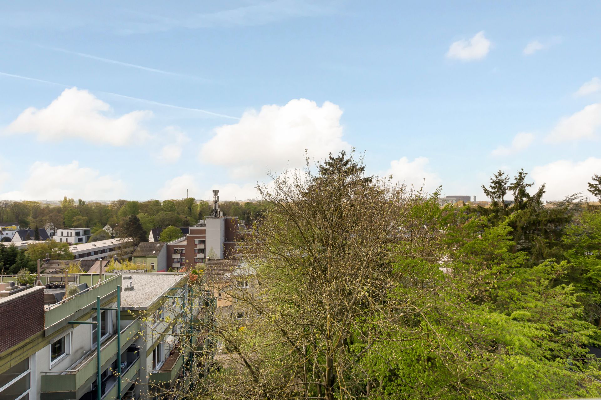 Blick auf Wohngebäude, Bäume und blauen Himmel mit einigen Wolken.