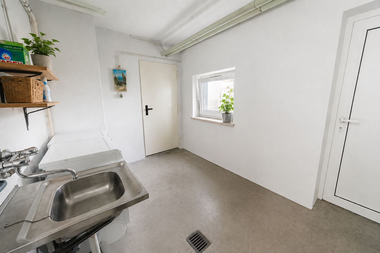 Heller Raum mit Waschbecken, Regalen, kleinem Fenster und zwei Türen.