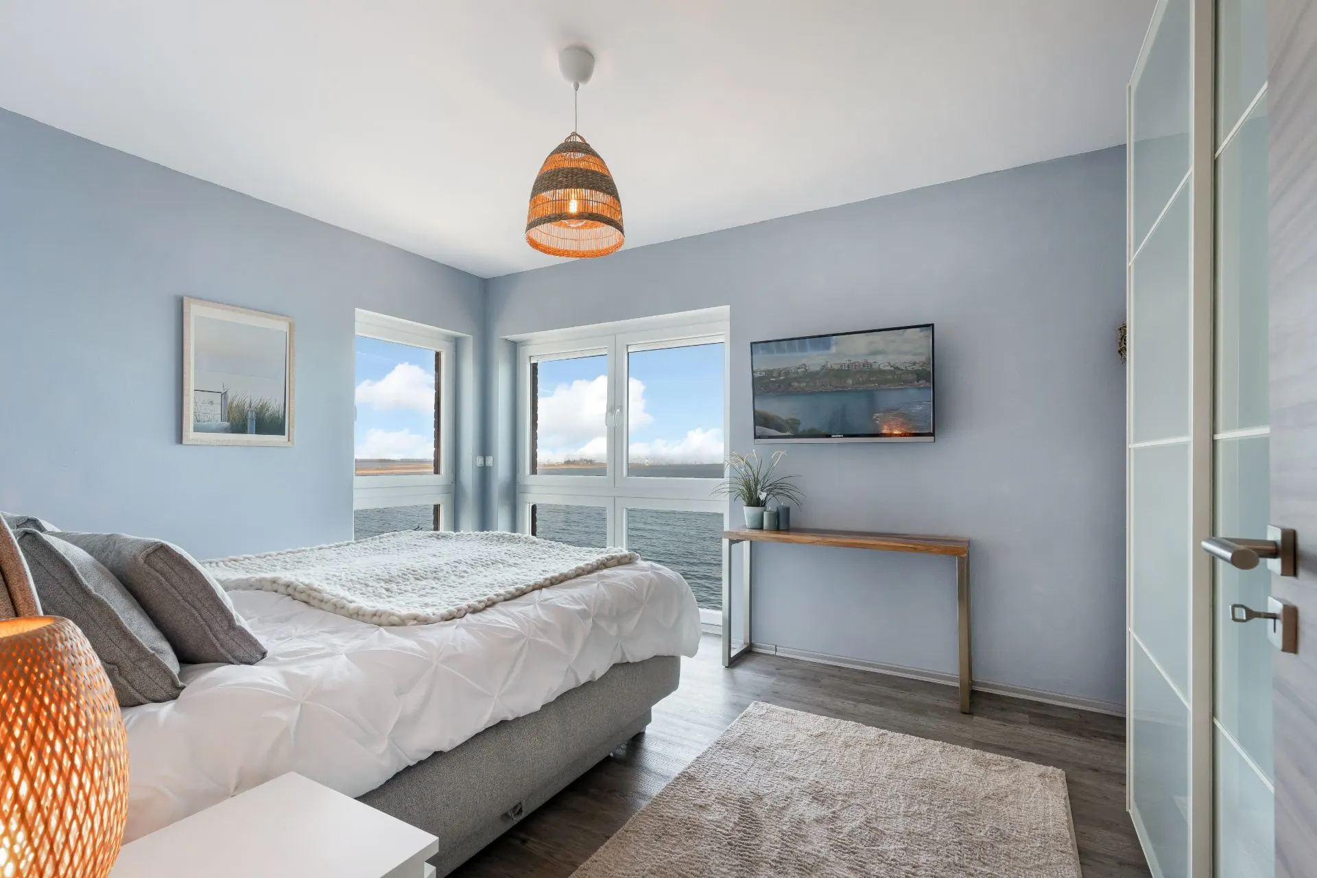Modernes Schlafzimmer mit großem Bett, blau gestrichenen Wänden und Panoramablick aufs Wasser.