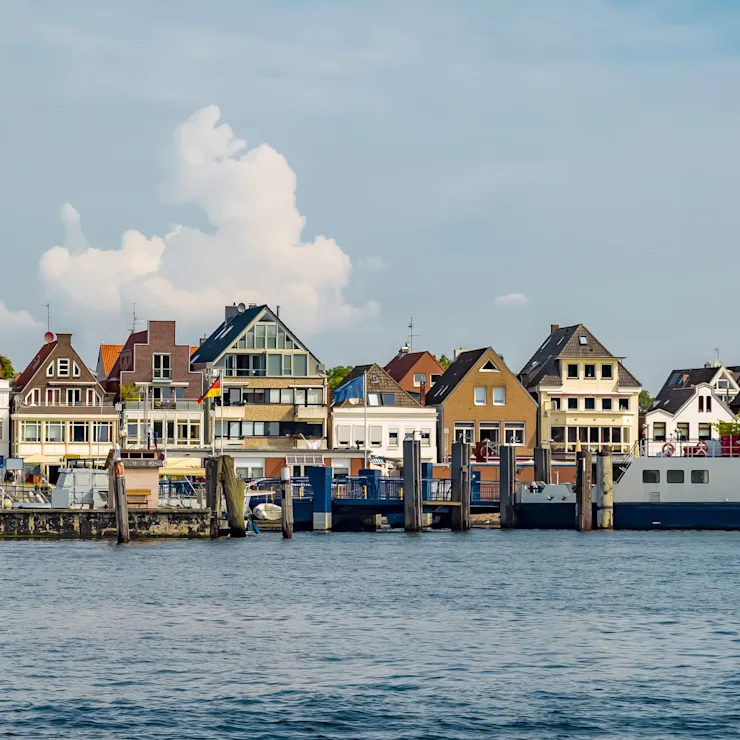 Mehrere Wohnhäuser und Gebäude an einer Uferpromenade mit Booten vor dem Wasser.