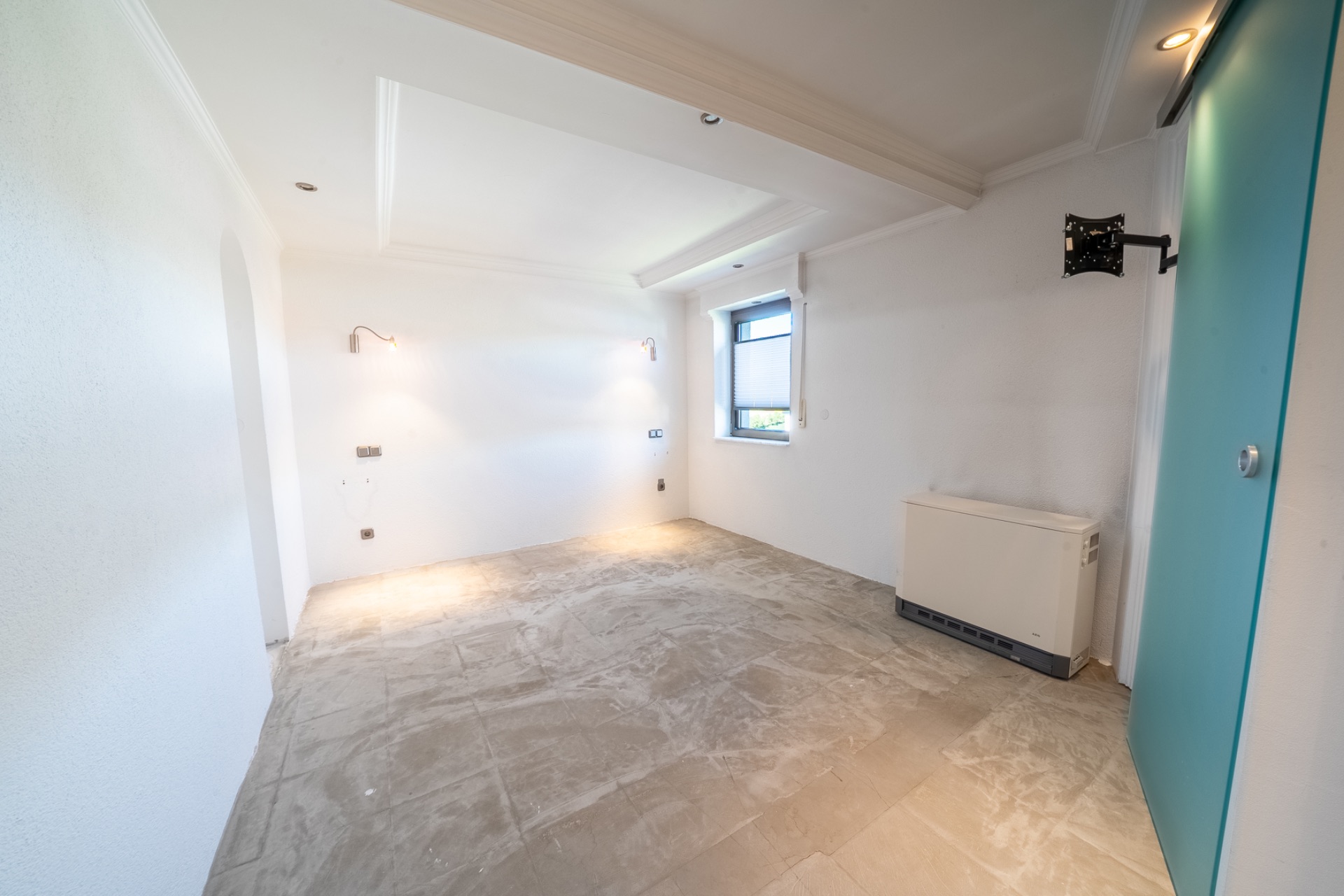 Leerer, heller Raum mit weiß gestrichenen Wänden, einem Fenster und einem Heizkörper.