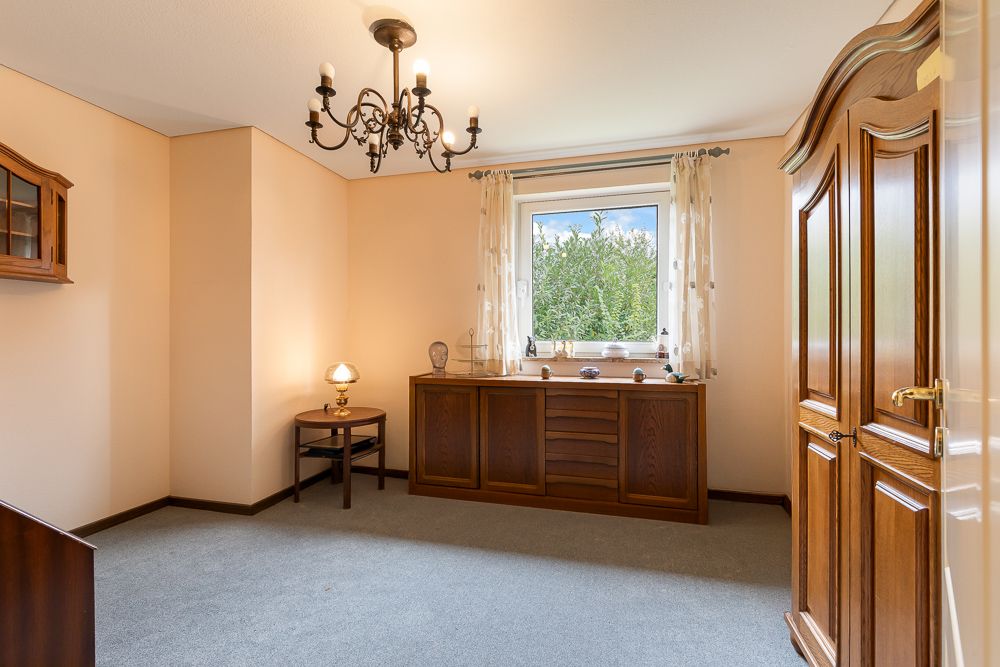 Hell eingerichtetes Zimmer mit Holzschrank, Kommode, Fenster und Kronleuchter.